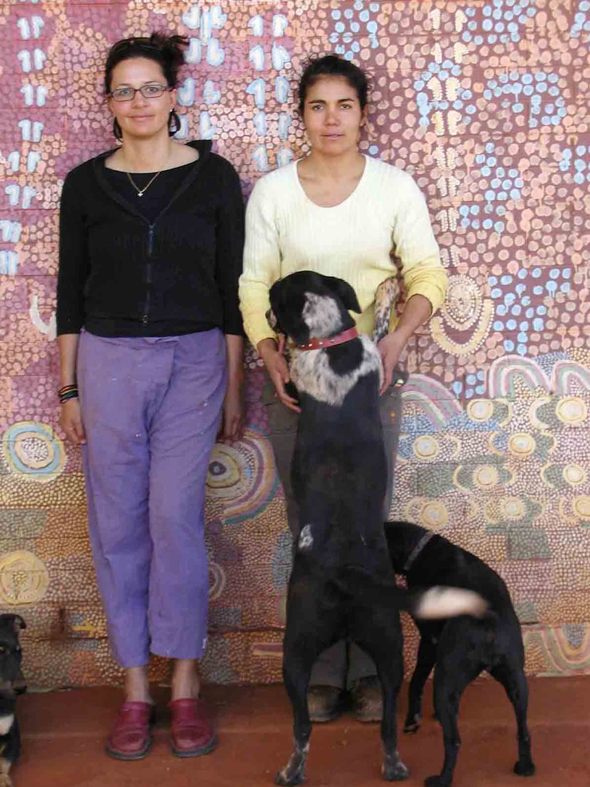 Two women leaning against a wall with two dogs.