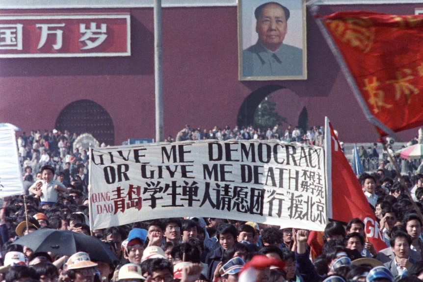 A huge crowd in Tiananmen Square holding up a banner reading "Give Me Democracy or Give me Death"