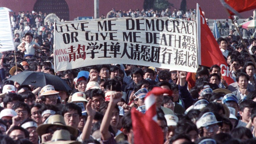 A huge crowd in Tiananmen Square holding up a banner reading "Give Me Democracy or Give me Death"
