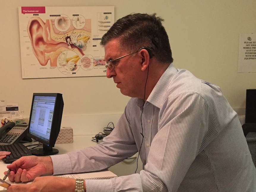 A man with a cochlear implant sits in a doctor's office in front of a diagram of the inner ear.