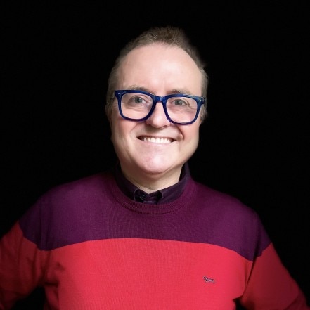 A man wearing glasses and a red and purple jumper