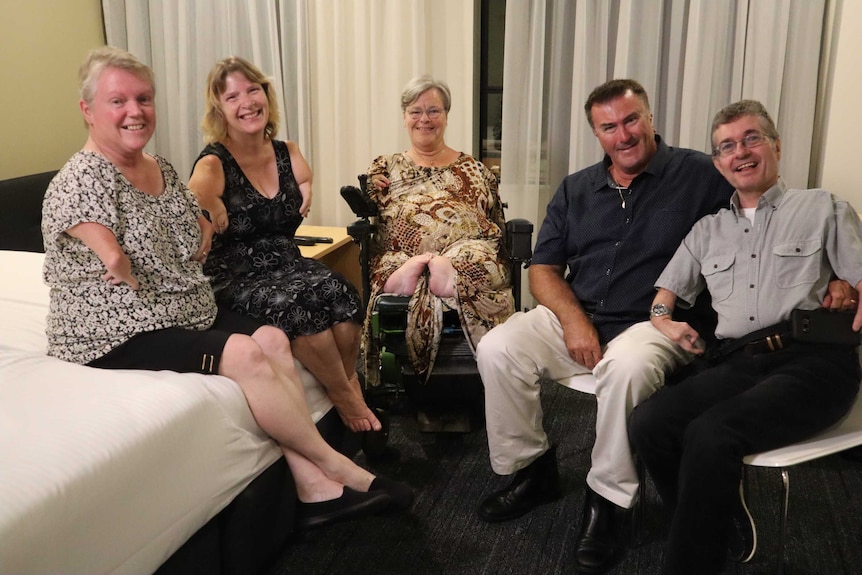 A group of men and woman sit in a semi-circle in a hotel room