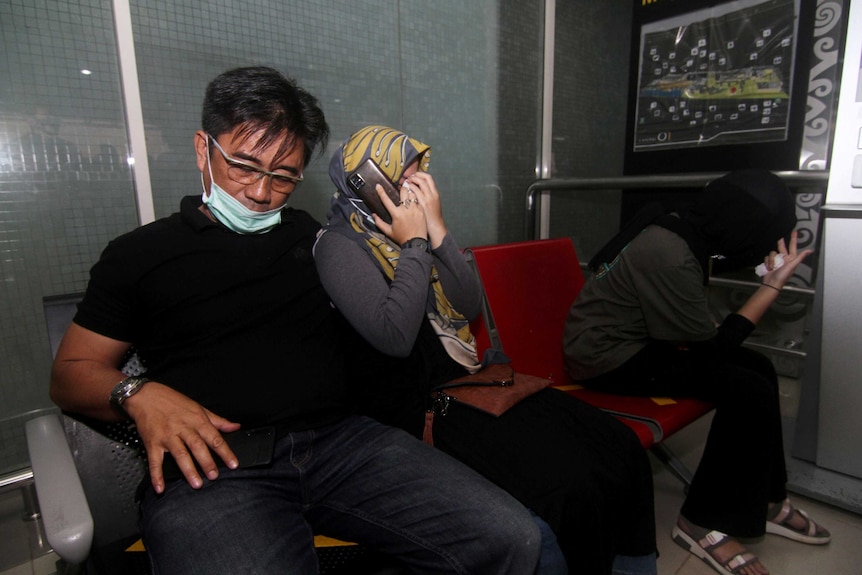 Family members cry and shield their face while talking on a phone at an airport