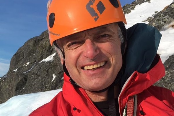 Climber Martin Moran on a snowy mountain wearing an orange helmet and red jacket.