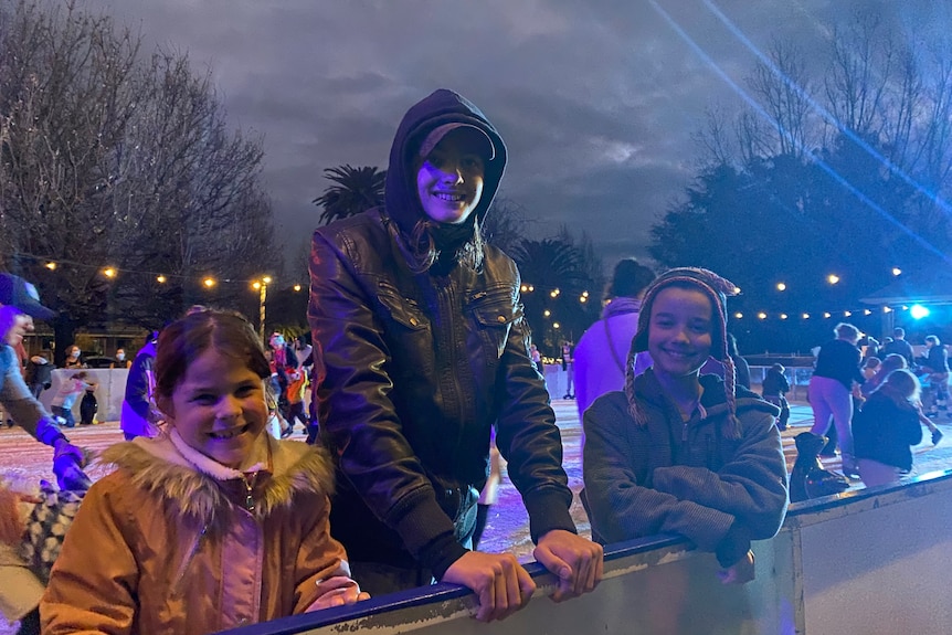three kids smiling on ice skating rink