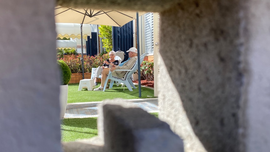 A retired couple sit on garden furniture under an umbrella in a photo framed by the raw edges of a cement building block.