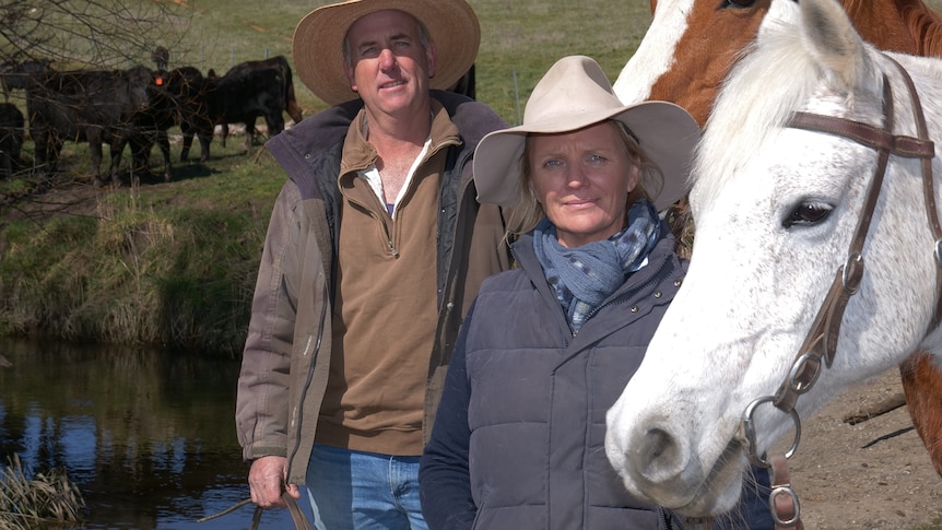 A man and woman look at the camera with their horses