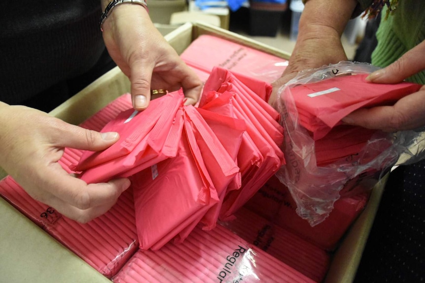 Two pairs of hands holding bright pink sanitary products.