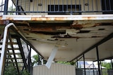 The underneath of a defective house visibly deteriorating, including some floorboards and piping that appears damaged.