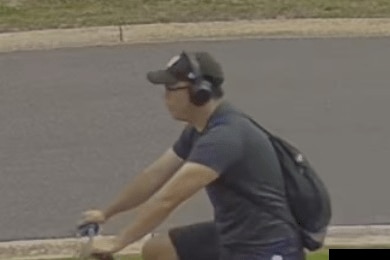 A capture from CCTV footage of a man riding a bike down a street.