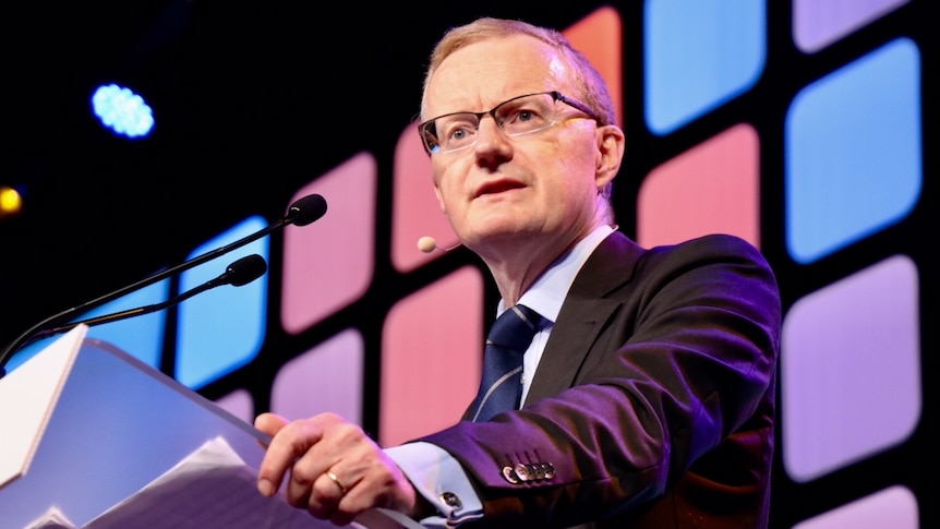 Philip Lowe stands at a lectern with a microphone. Behind him is a screen with multi-coloured squares