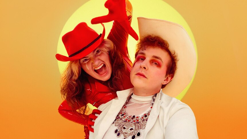 Two members of Cry Club on a yellow background. Heather wears red, Jono wears white, both have cowboy hats. 