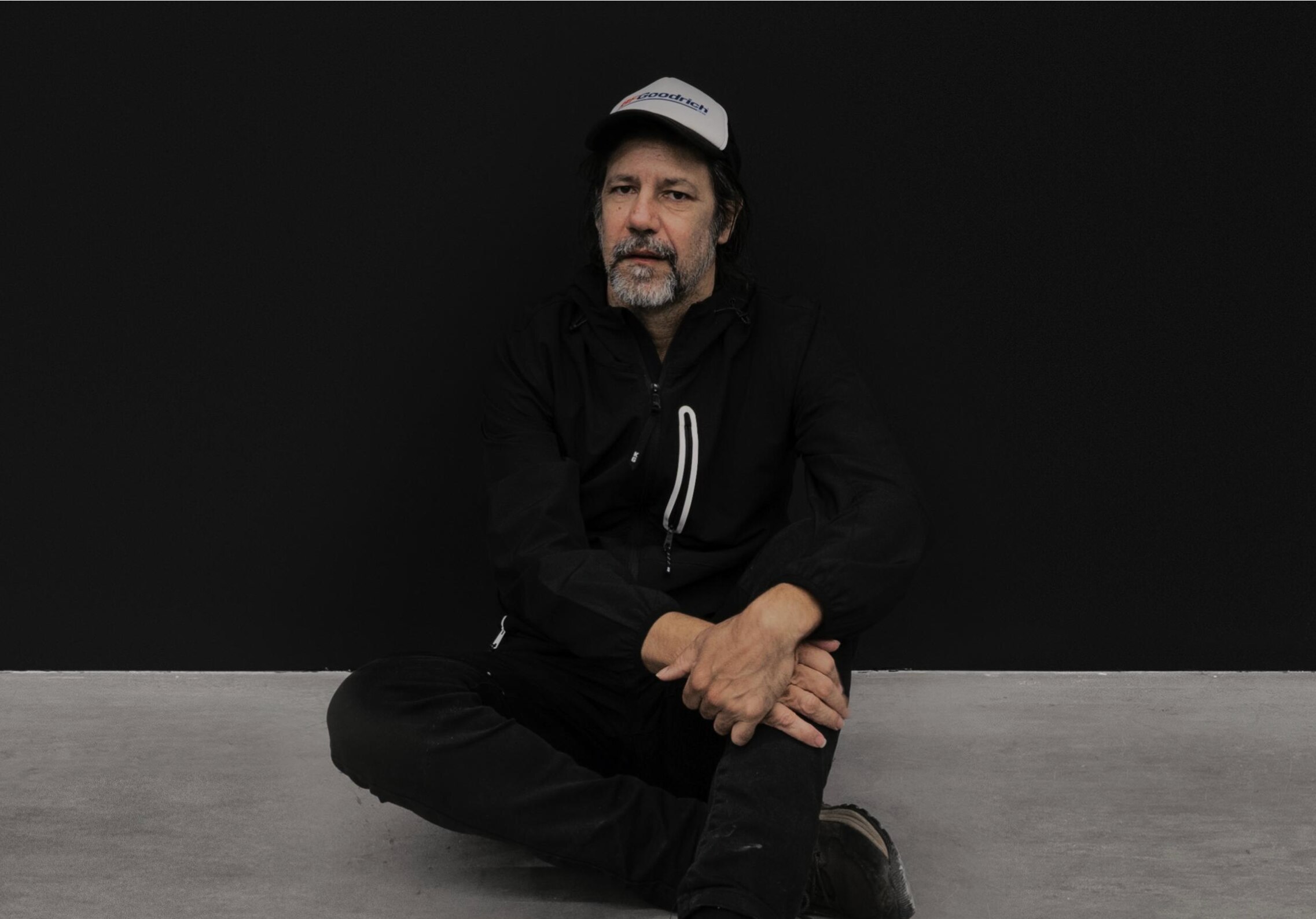 Artist Archie Moore sits on the ground in front of a blackboard wall.