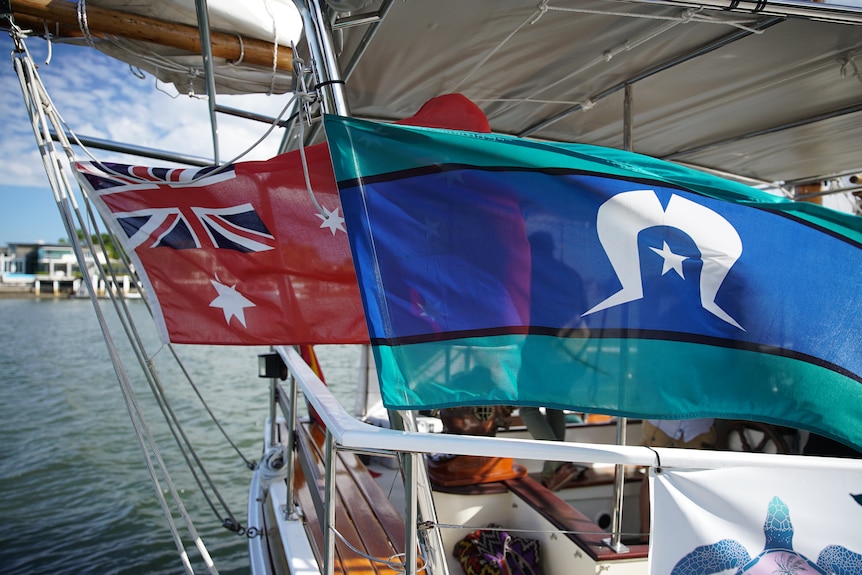 The Australian naval flag and the Torres Strait Island flag fly side by side on a ship.