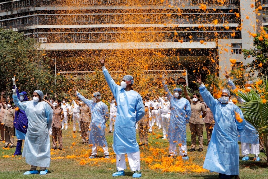 Nurses and doctors in India are standing as orange flower petals are sprayed over them.