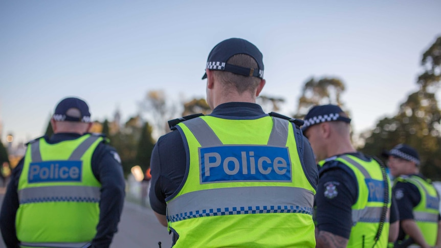 Police officers stand with their backs to the camera.