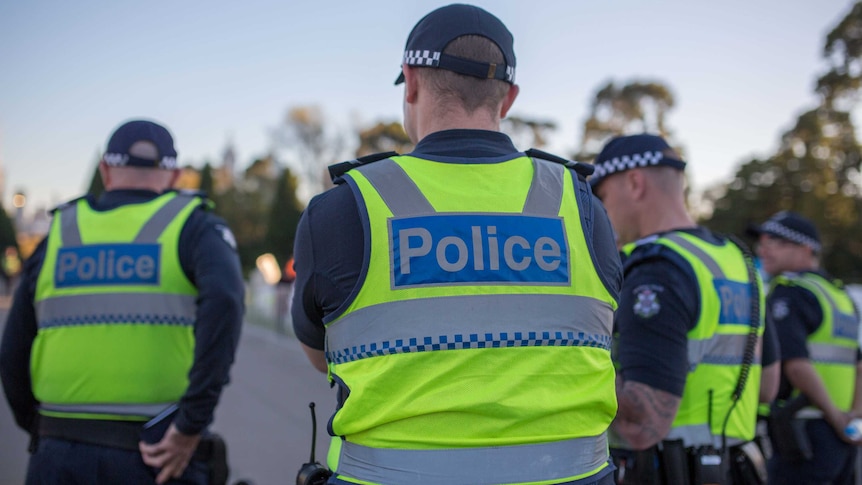 Police with high visibility vests stand with their back turned to the camera