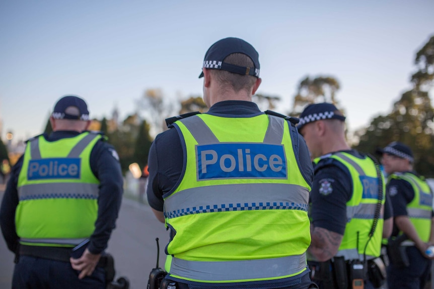 Victoria Police officers face away from the camera wearing high-vis vests.