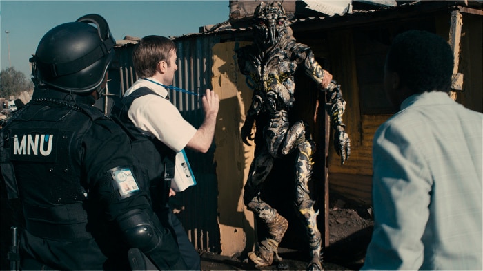 Photo of Sharlto Copley in front of an alien in the film District 9.