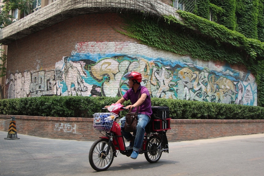 A courier on a motorbike riding through an urban street