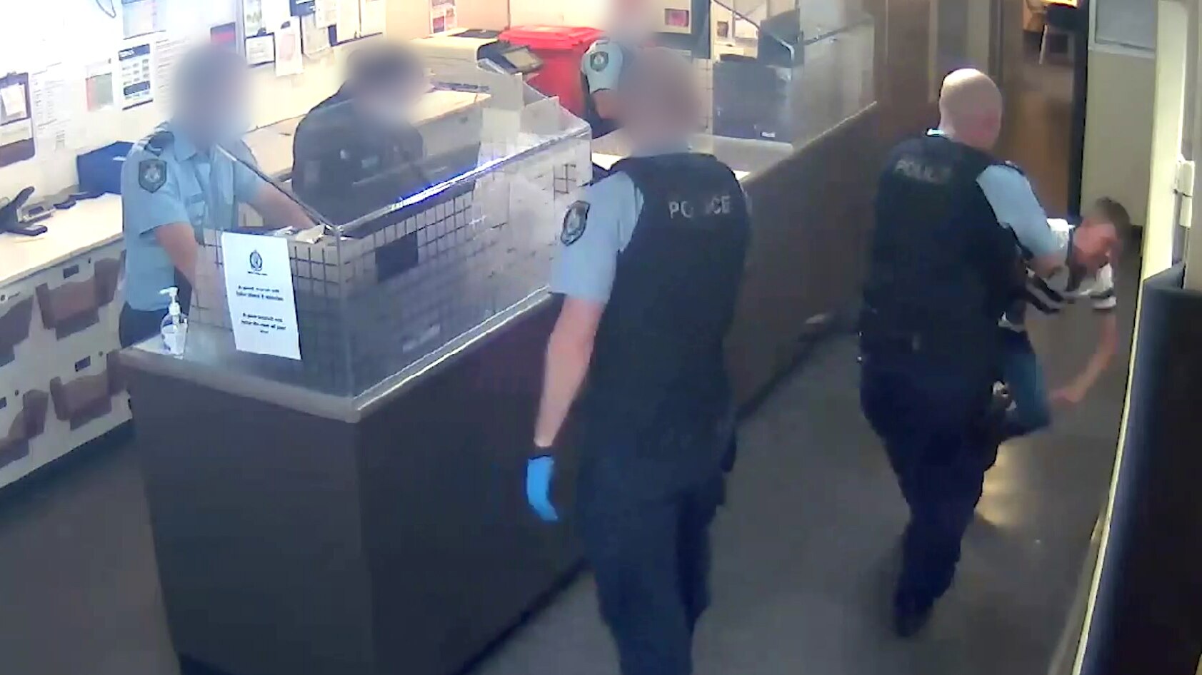 A still from CCTV footage of a man being thrown by a police officer across a police station area.