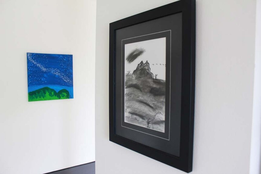 A charcoal painting hanging from the kitchen wall. A mountain and track is visible in the frame.