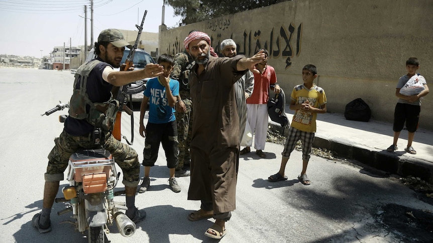 A member of the Syrian Democratic Forces (SDF) indicates a safe street to civilians fleeing IS zones in Manbij, northern Syria.