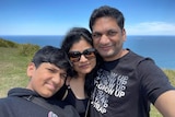 A boy next to his mother and father taking a selfie with on the coast.