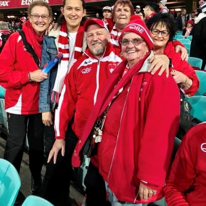 A group of six Sydney Swans' fans dressed in clubs colours pose for a photo from their seats at a game