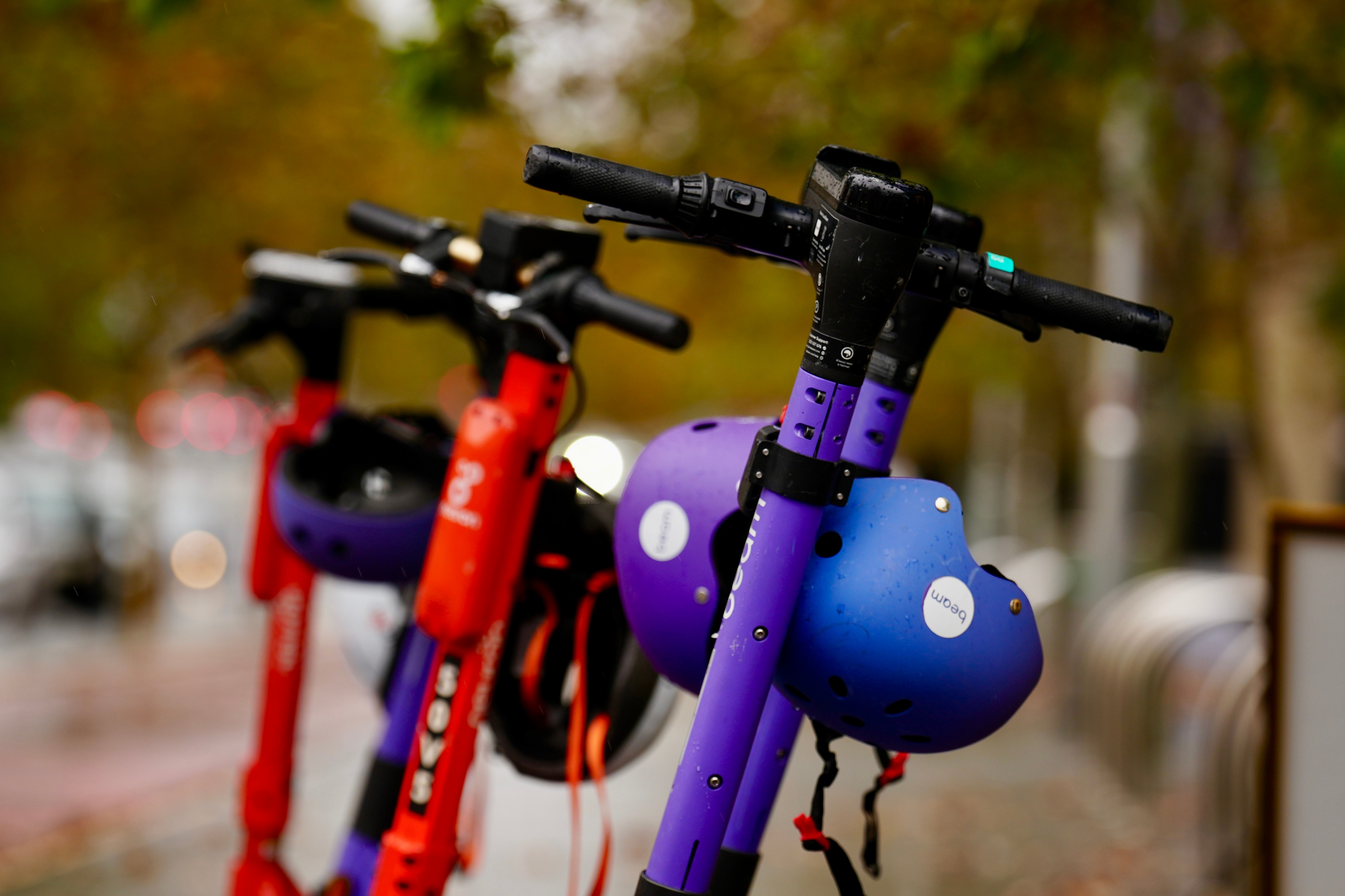 特写镜头：几辆电动滑板车的车把上挂着头盔。