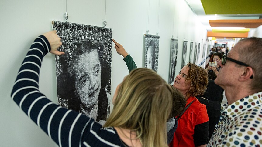 Colour photo of hospital hallway full of families looking at artworks at A Little Piece of Me exhibition.