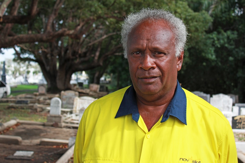 Elton wearing a bright yellow Nova Skills shirt with gravestones in the background