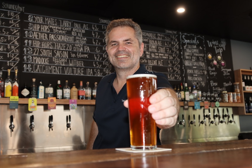 A bartender smiles as he hands over a beer.