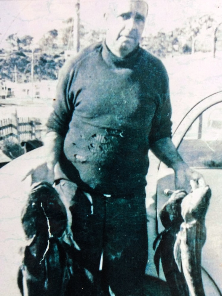 Black and white portrait from c. 1960s of man in torn woollen jumper holding three large flathead