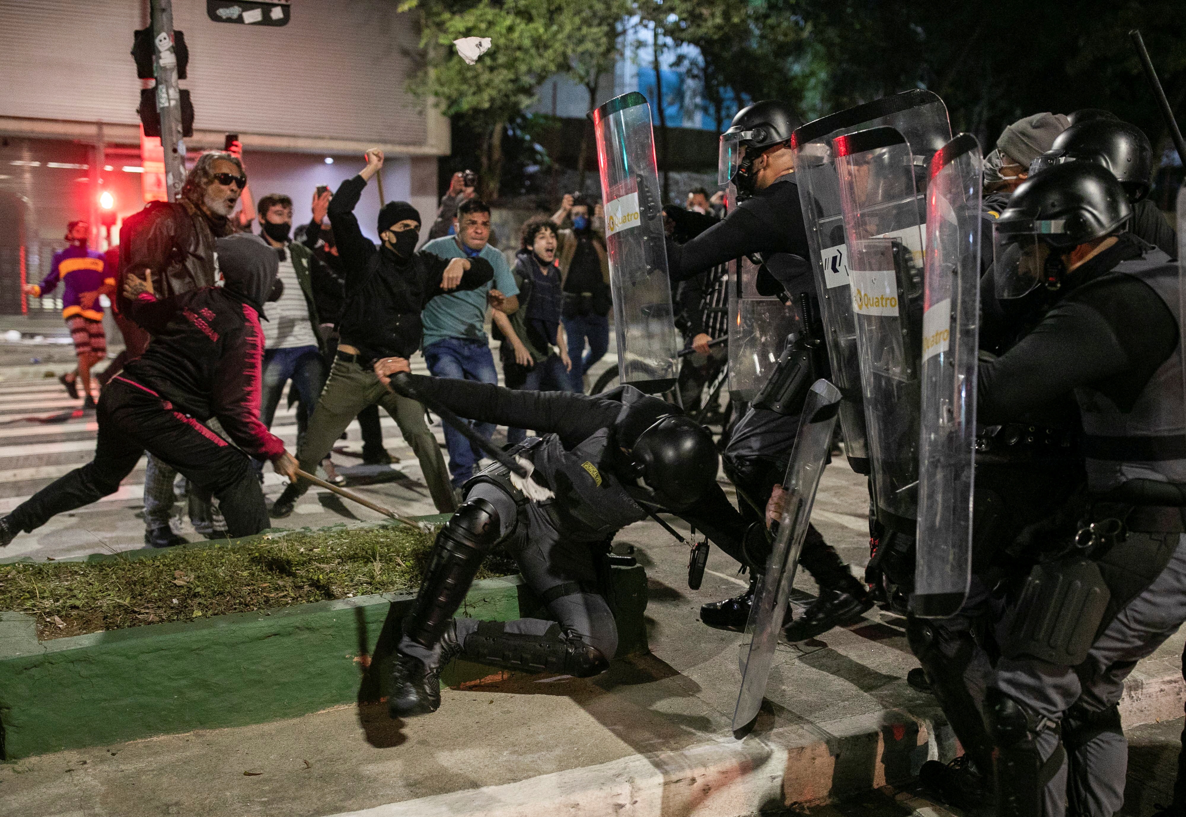 Riot police hold shields in front of protesters with their fists up 