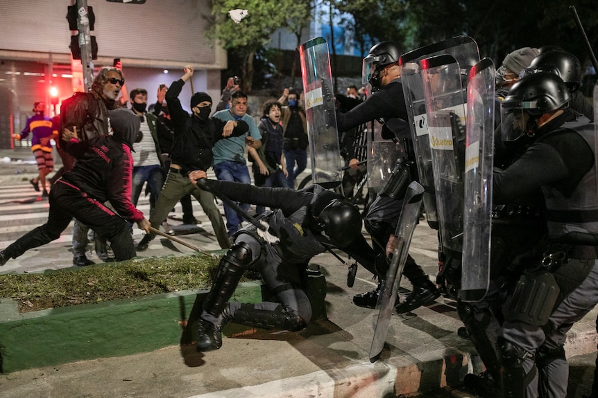 Riot police hold shields in front of protesters with their fists up 