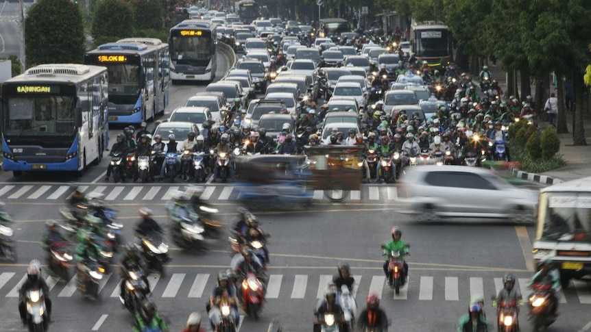 A six-lane highway choked with buses, cars and bikes all driving in the same direction and cars rushing past at intersection.