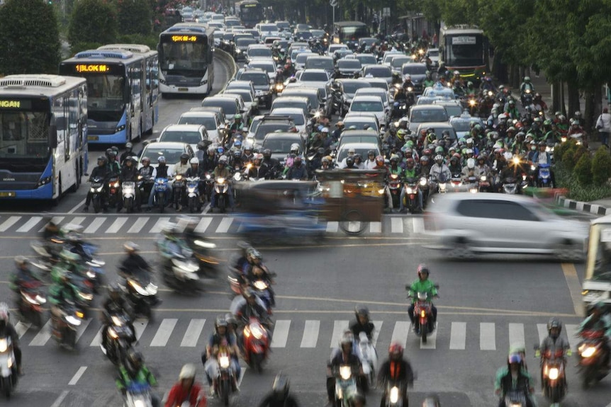 A six-lane highway choked with buses, cars and bikes all driving in the same direction and cars rushing past at intersection.