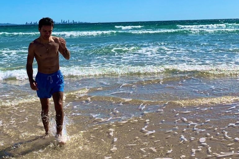 A man walks out of the ocean with a gold coast skyline behind him