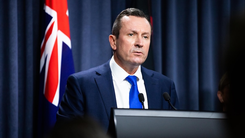 Man speaks at lectern in front of Australian flag.