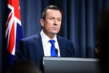 Man speaks at lectern in front of Australian flag.