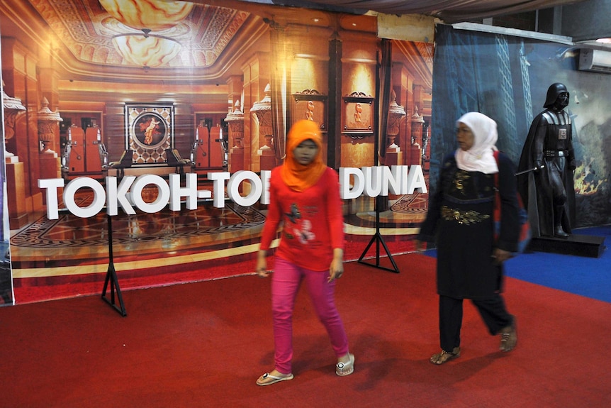 Visitors walk past an empty exhibit space at a museum.