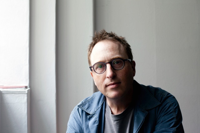 A man with glasses in a shirt looks at the camera