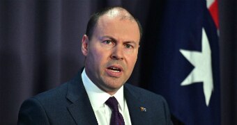 Josh Frydenberg making a speech, wearing a suit with an Australian flag while standing in front of an Australian flag.