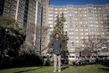 Barry stands on the grass, with the large apartment complex towering in the background