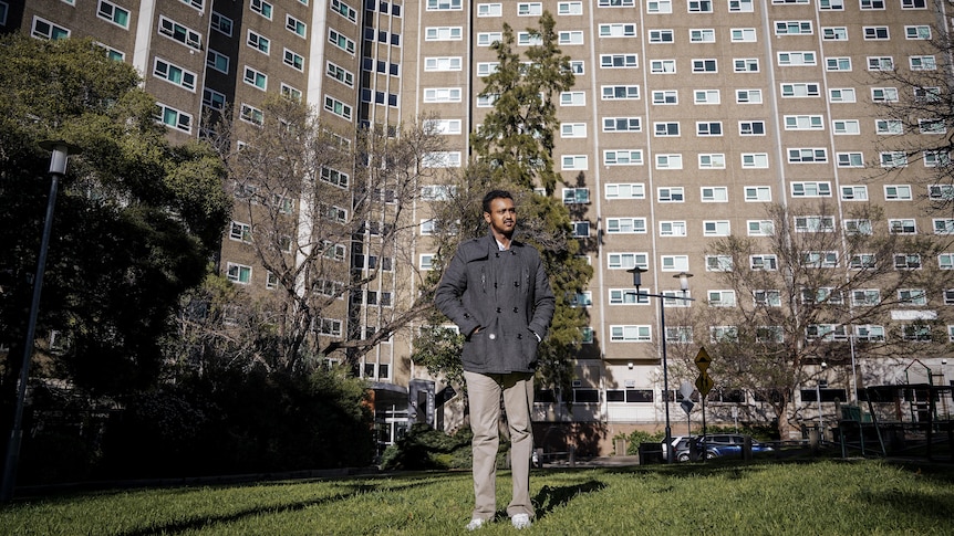 Barry stands on the grass, with the large apartment complex towering in the background