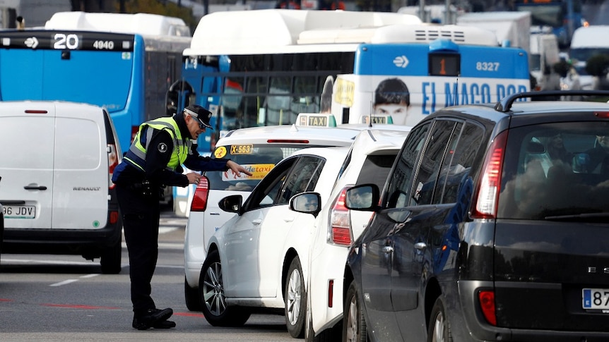 A uniformed police officer gestures as directs the driver of a small car that is part of a long queue of vehicles