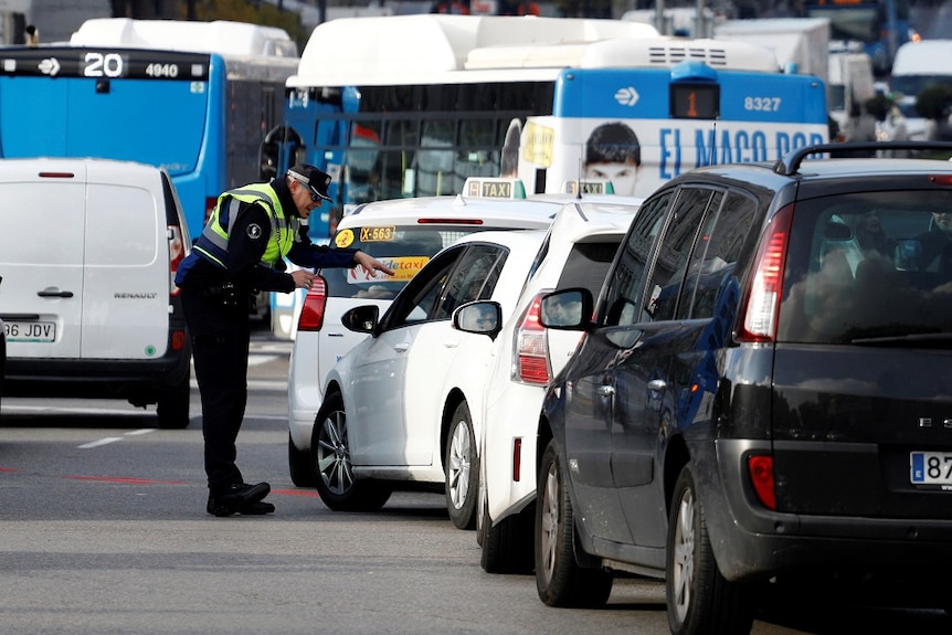 A uniformed police officer gestures as directs the driver of a small car that is part of a long queue of vehicles