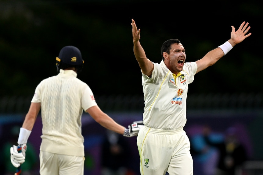 Scott Boland stands with his arms wide apart as an English batter stands with his back to him