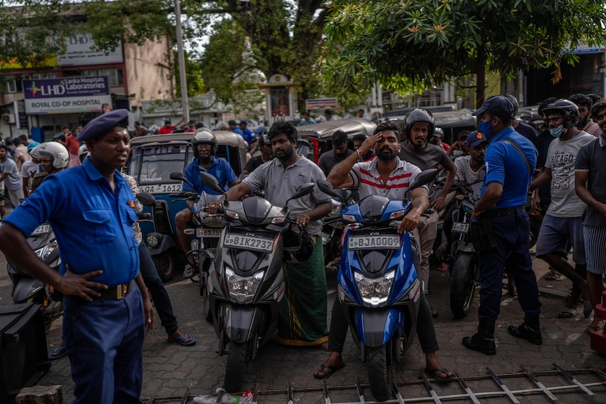 Los policías montan guardia mientras la gente hace cola para comprar gasolina